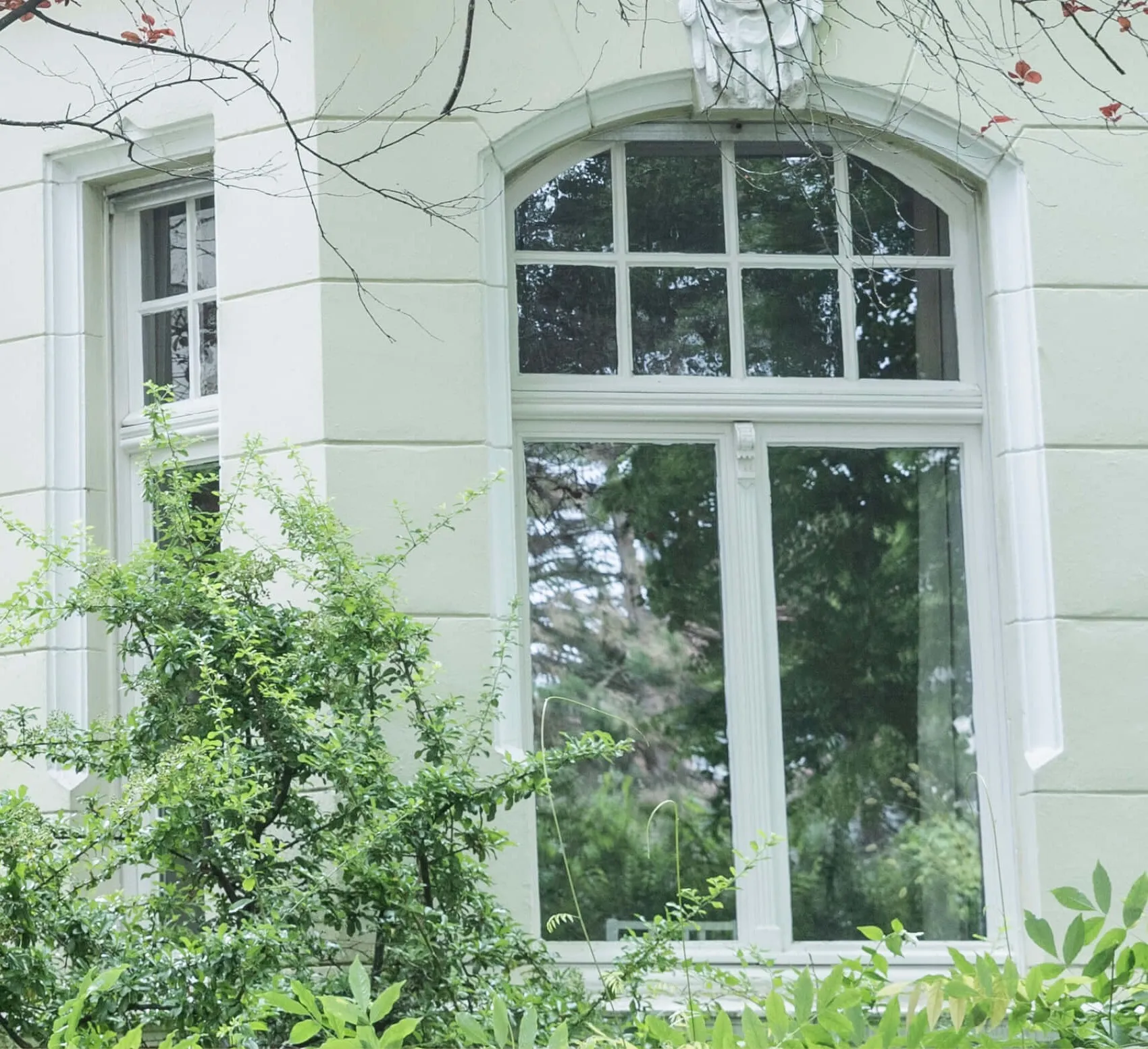 Rundbogenfenster einer hellen Villa im Grünen